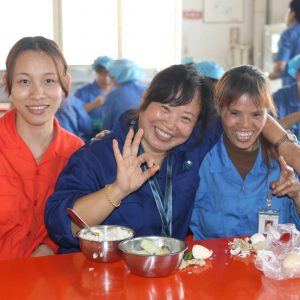 Three smiling Chinese ladies in a factory canteen.