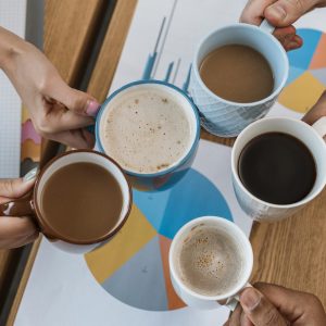 Five people clinking their cups of coffee in an office environment, seen from above.