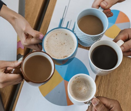 Five people clinking their cups of coffee in an office environment, seen from above.